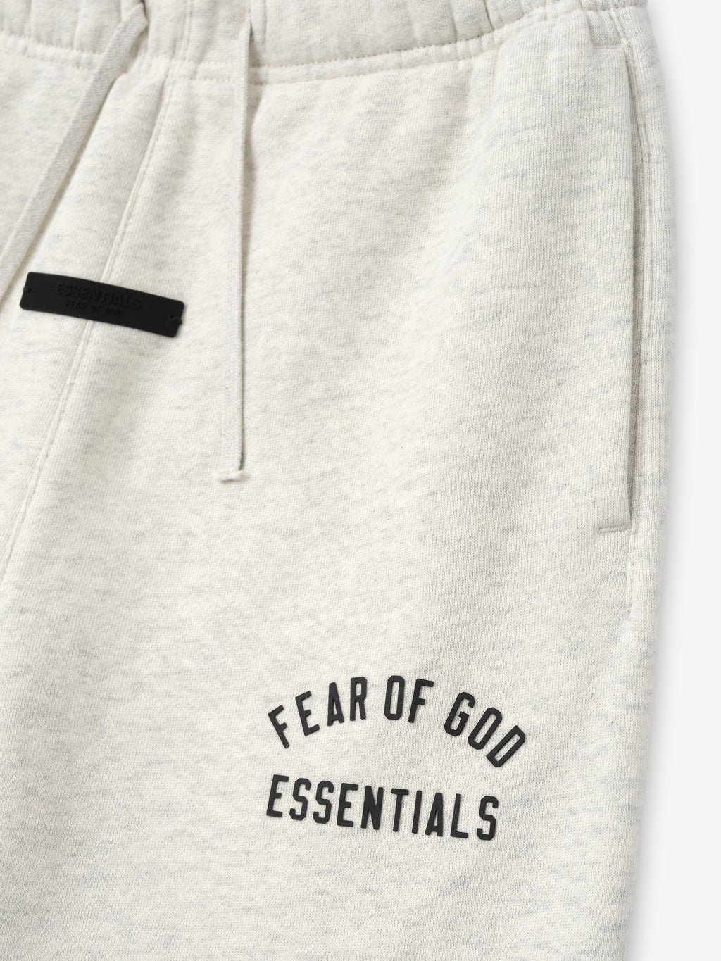 close-up of off-white kids sweatpant featuring black Fear of God Essentials text and drawstring waistband