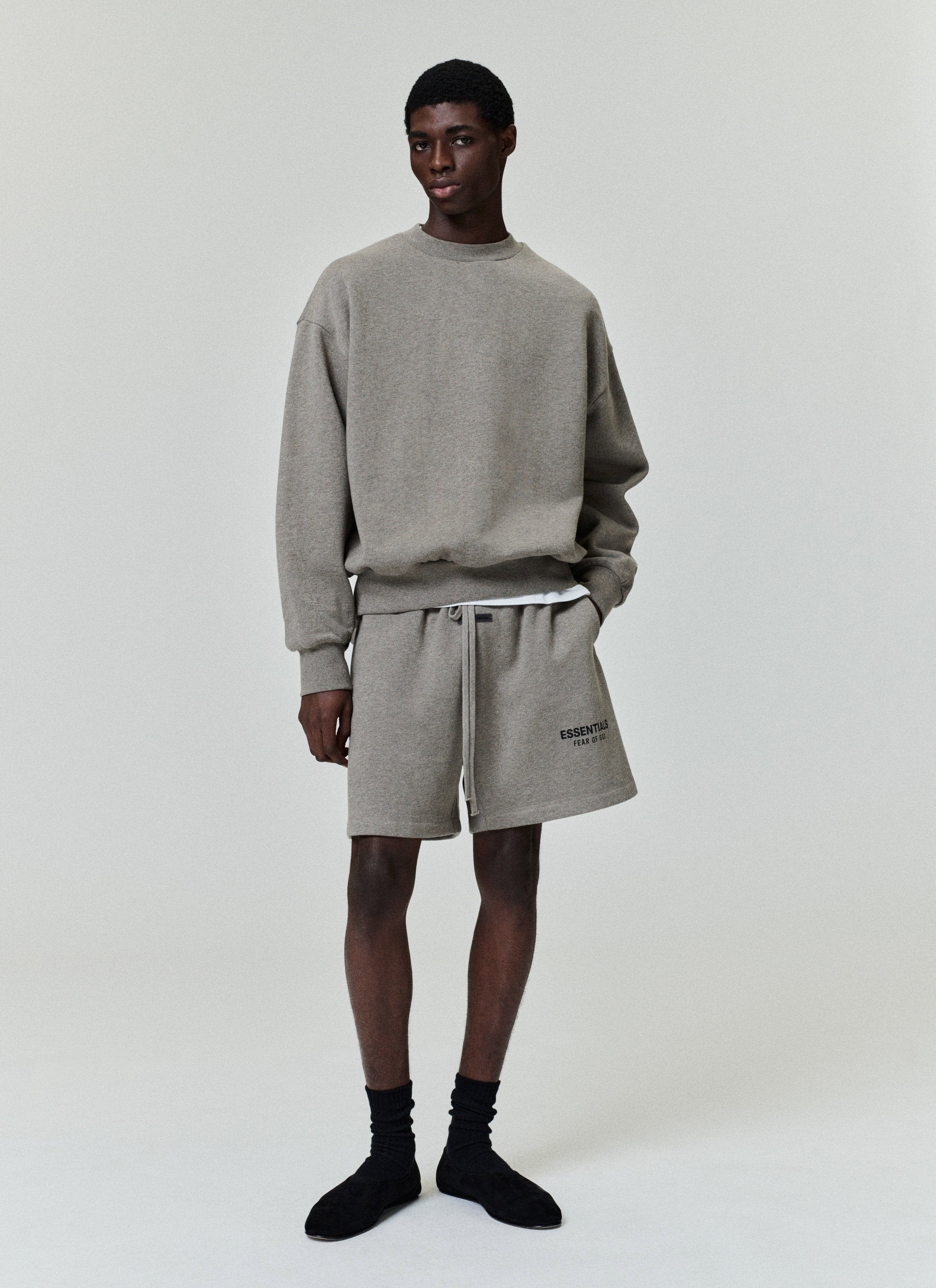 Taupe sweatshorts with adjustable drawstring, relaxed fit, side pockets, and small black "ESSENTIALS FEAR OF GOD" logo on leg