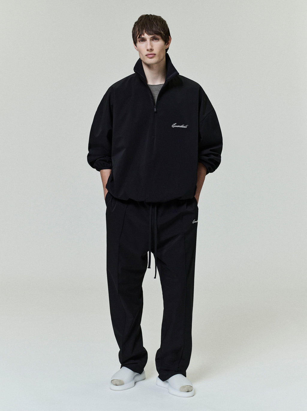Front view of model wearing black Sporty Nylon Half Zip with matching pants and white slides on plain background