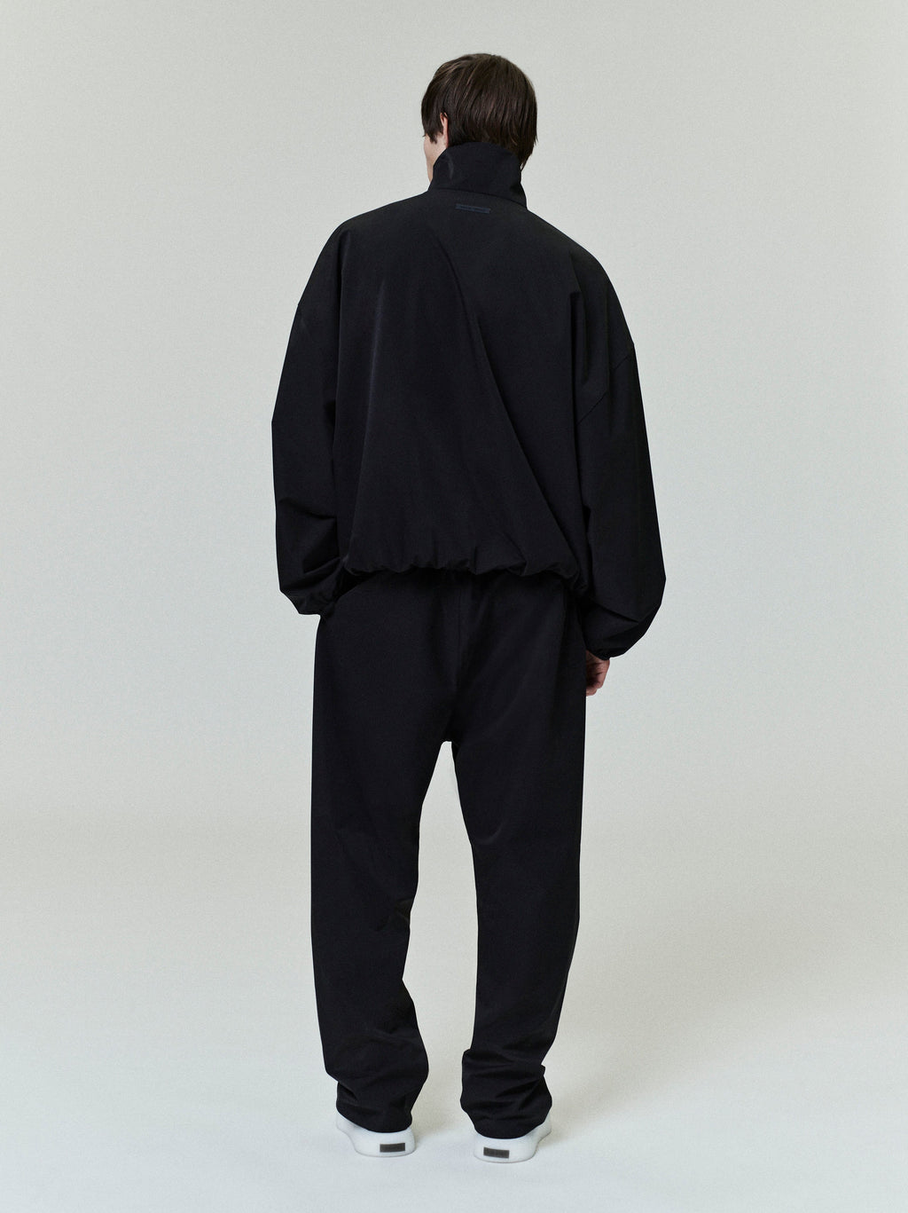 Rear view of model wearing black Sporty Nylon Half Zip jacket and matching pants against plain gray background