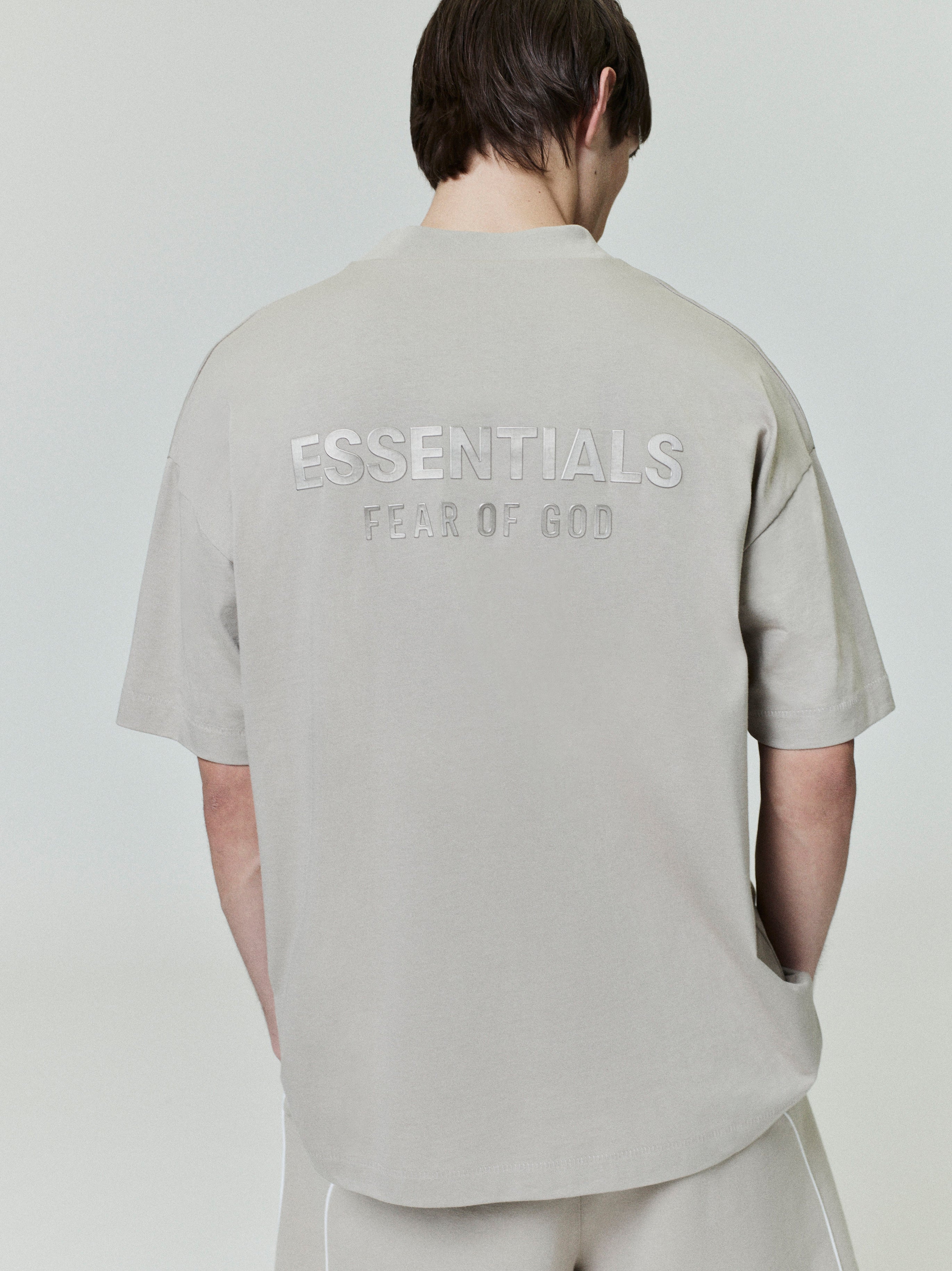 back view of light beige medium-weight cotton jersey tee with ESSENTIALS Fear of God embossed logo across upper back