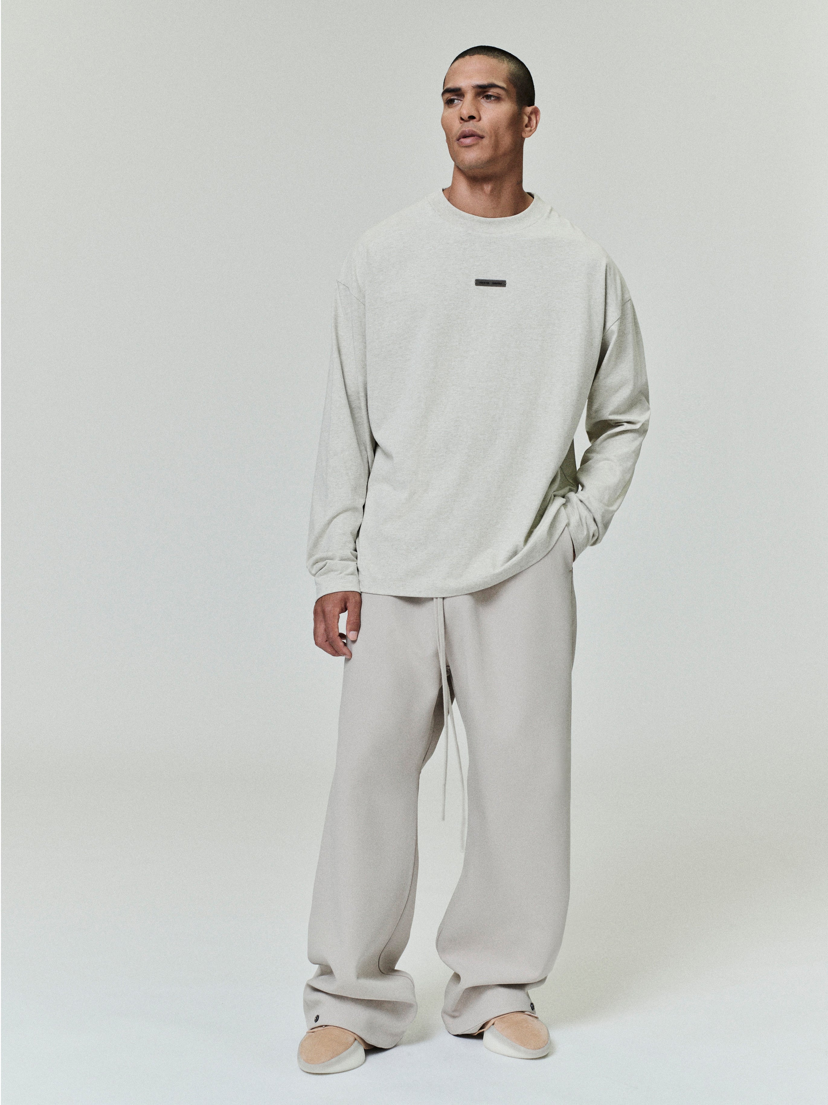 front view of light gray medium-weight cotton long sleeve tee with rib-knit crewneck and small rectangular logo patch on chest