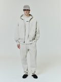 male model wearing light beige classic fleece zip-up hoodie with matching sweatpants and black slip-on shoes
