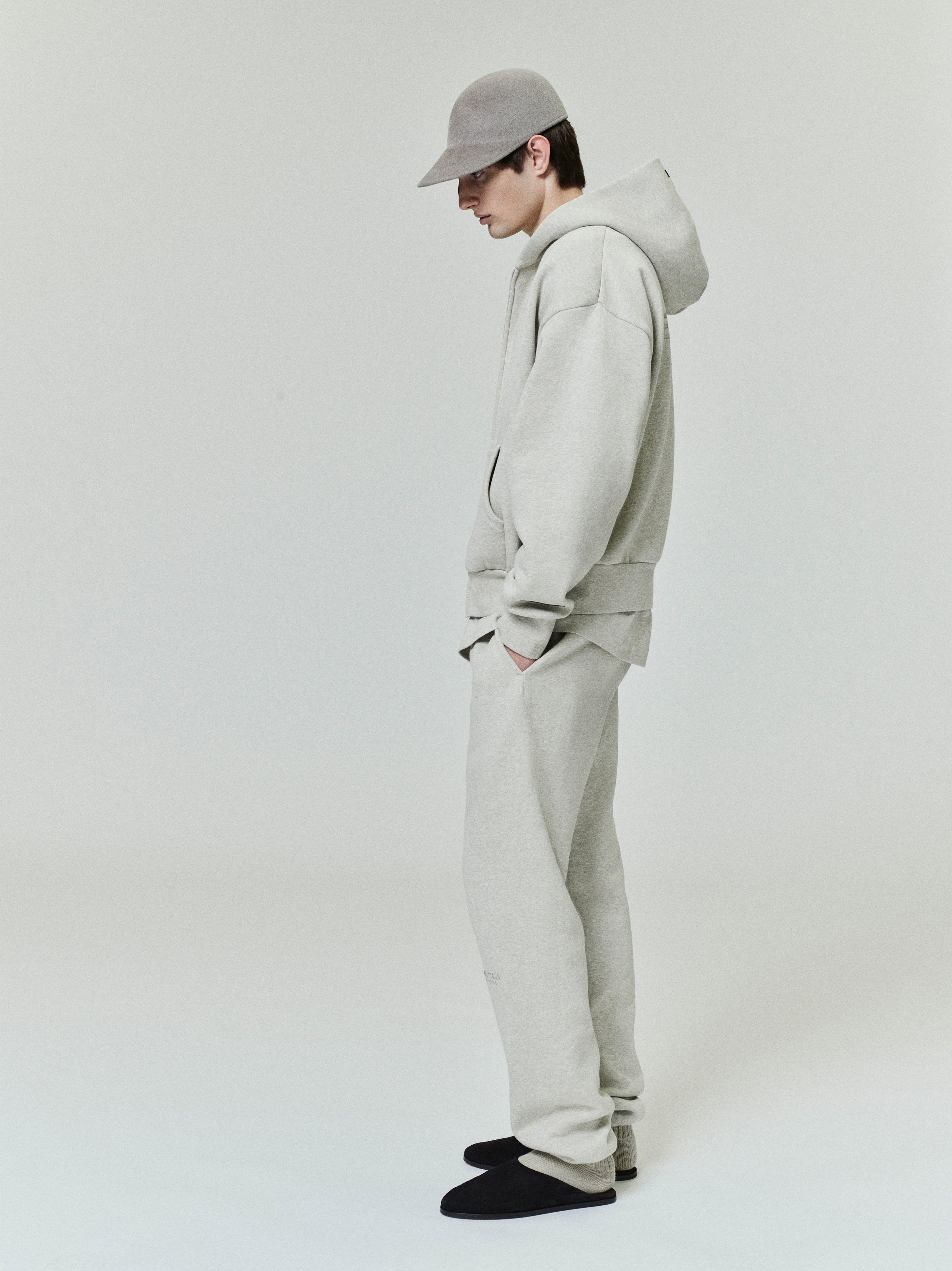 male model wearing light grey relaxed fit fleece zip-up hoodie with matching sweatpants and grey cap