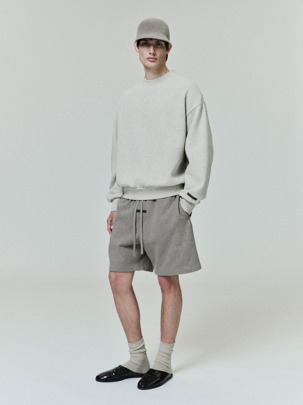 Full front view of model wearing light grey Classic Fleece Crewneck with taupe shorts, matching cap, and black loafers on neutral background