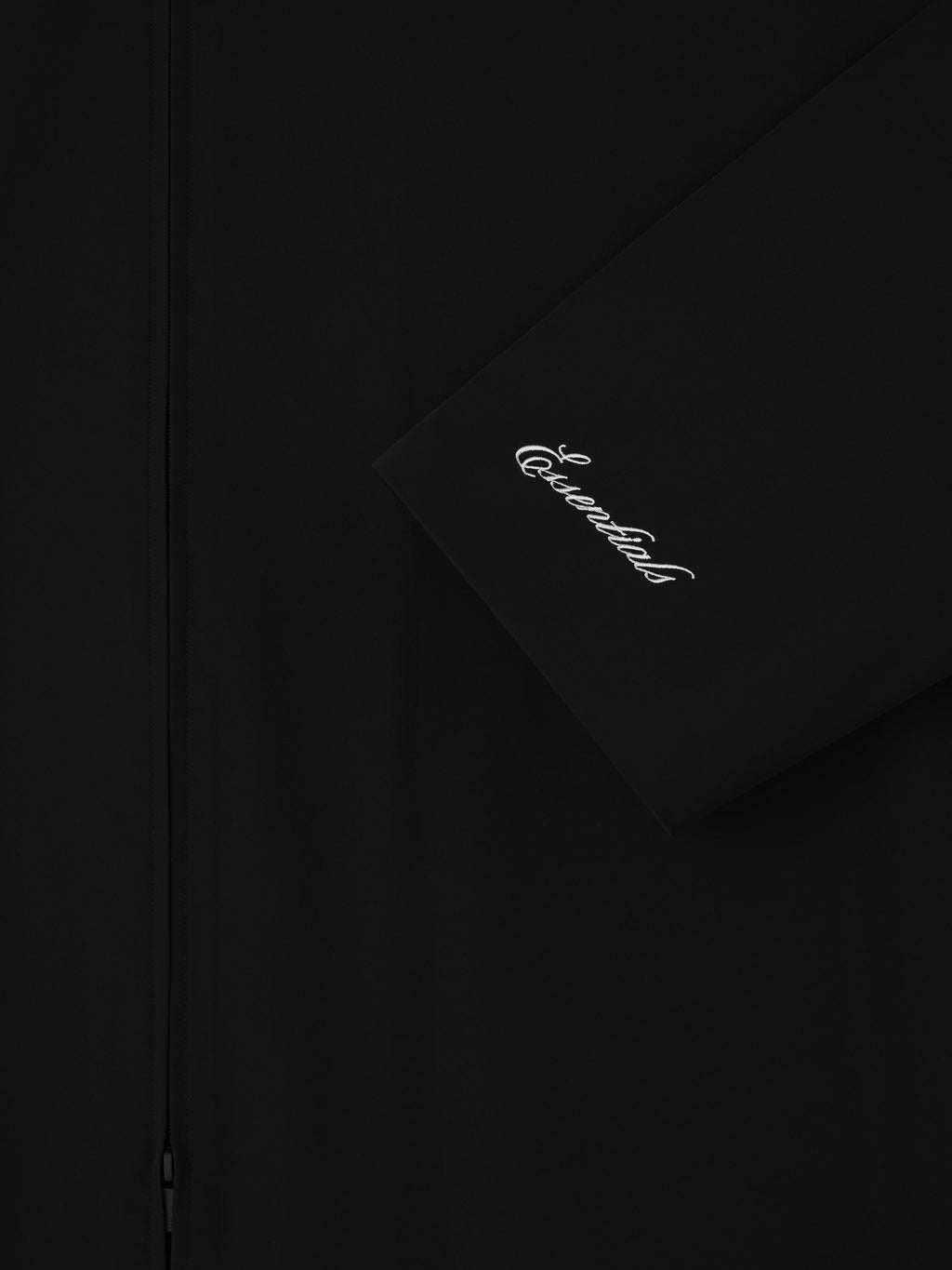 Close-up of black Sporty Nylon High Neck Jacket sleeve with white cursive Essentials logo embroidery and front zipper detail