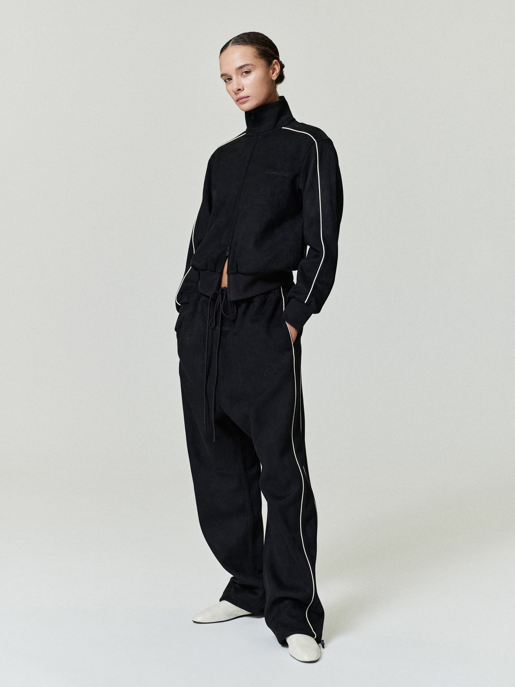 model wearing black bonded suede fleece relaxed pants and matching zip-up jacket with contrast piping details