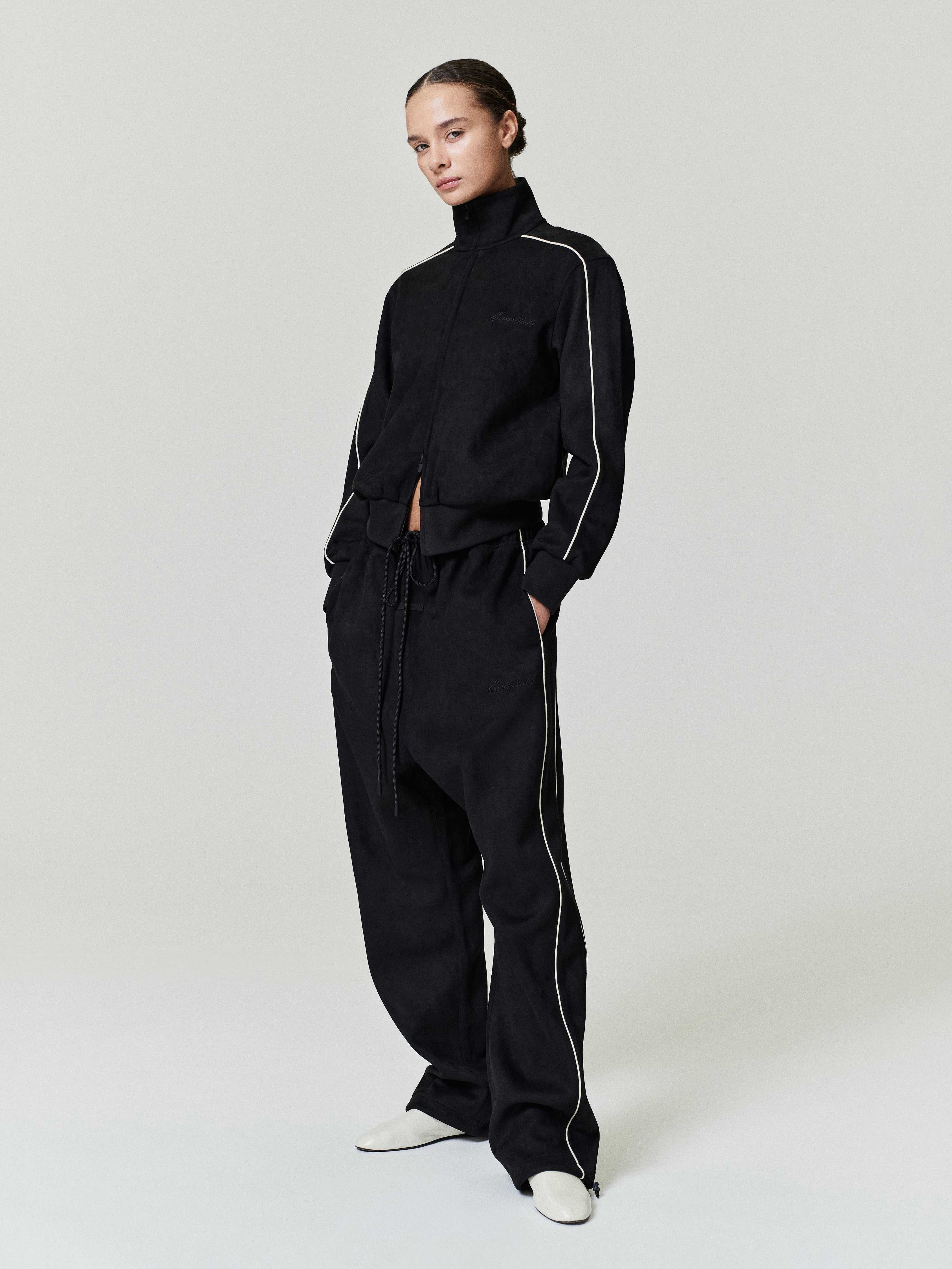 model wearing black bonded suede fleece relaxed pants and matching zip-up jacket with contrast piping details