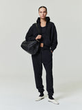 woman wearing black full zip hoodie with matching joggers and carrying a large textured black shoulder bag