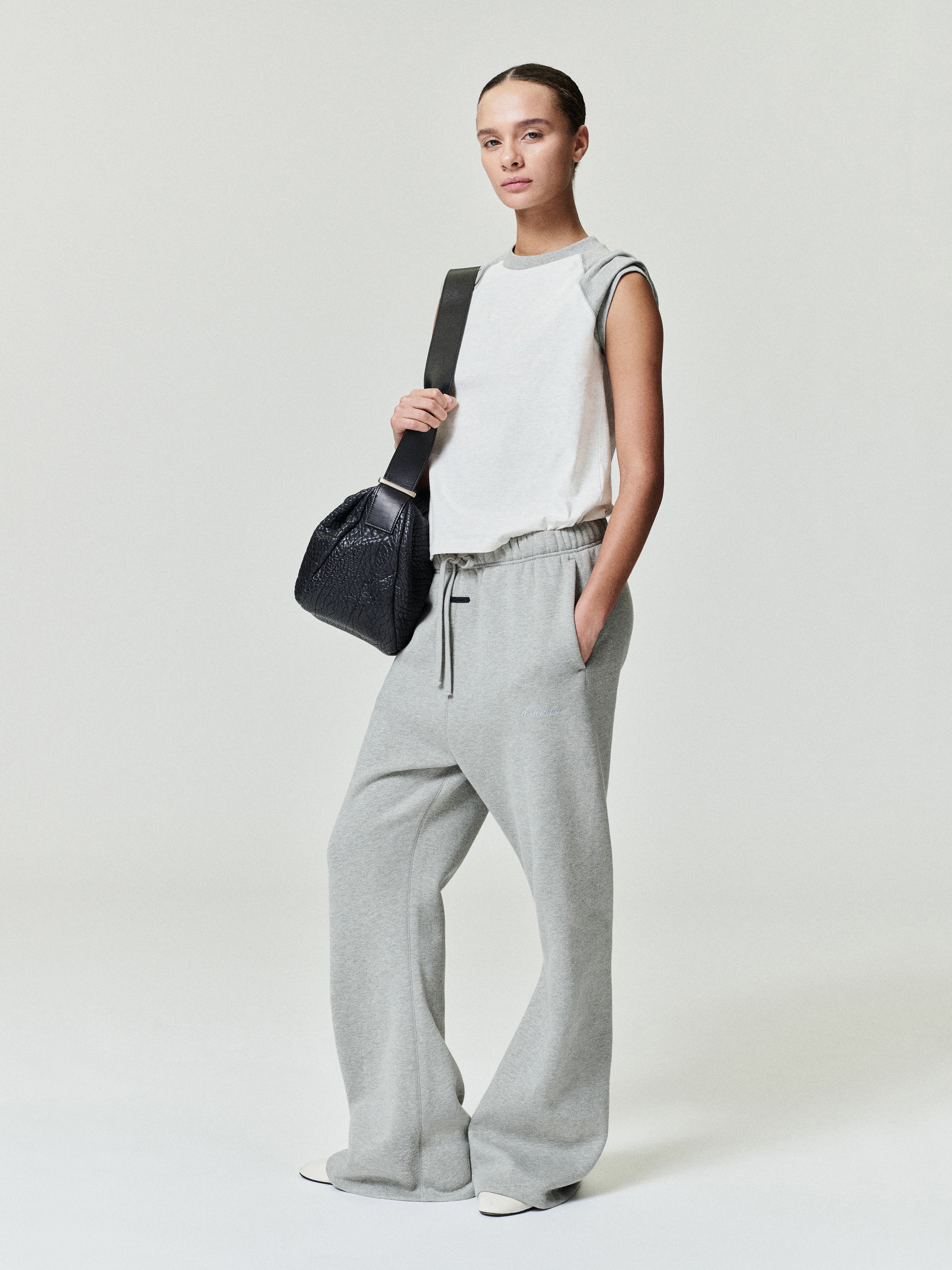 woman wearing sleeveless white ribbed cotton baseball tee with classic fit and raw hem paired with gray sweatpants