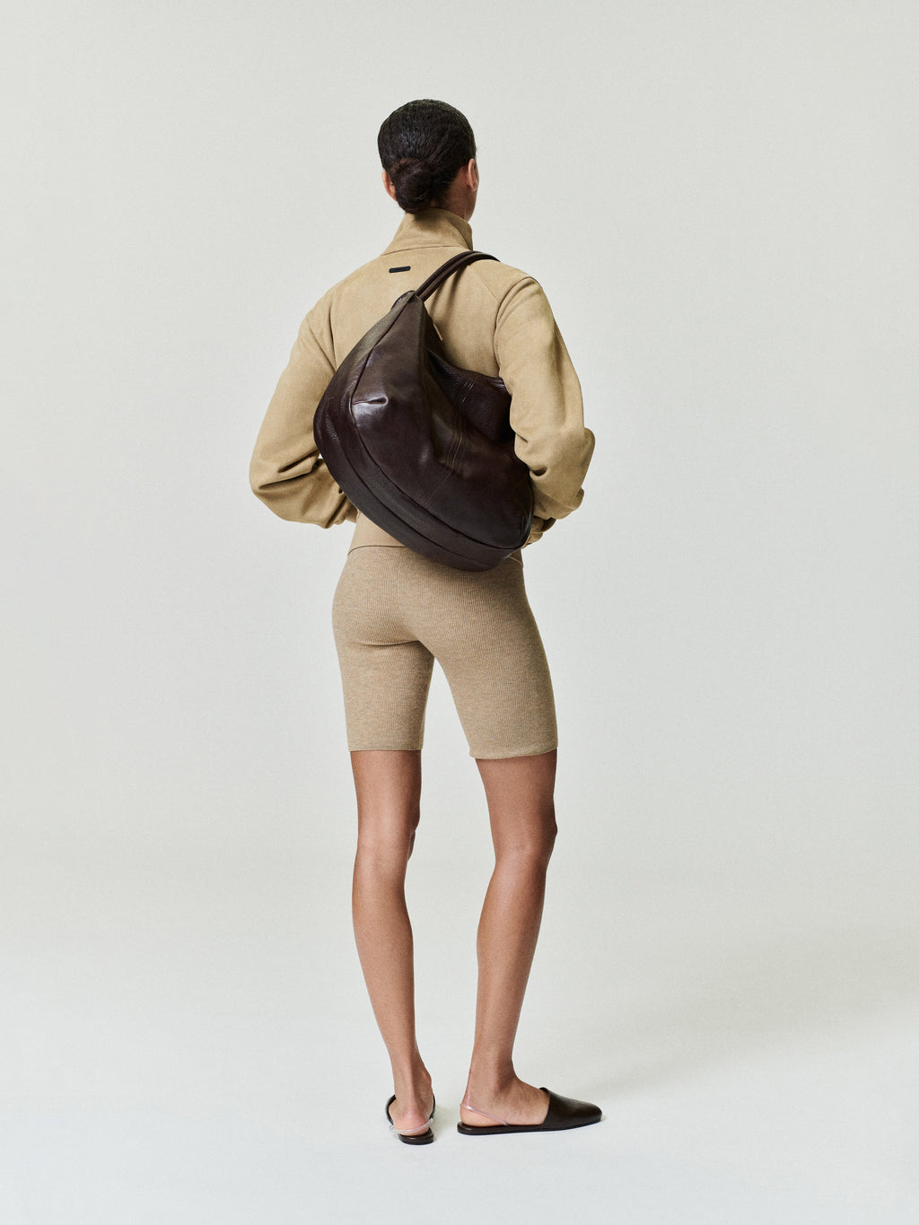 woman wearing beige ribbed knit bike shorts with high waist and mid-thigh length styled with matching jacket and large bag