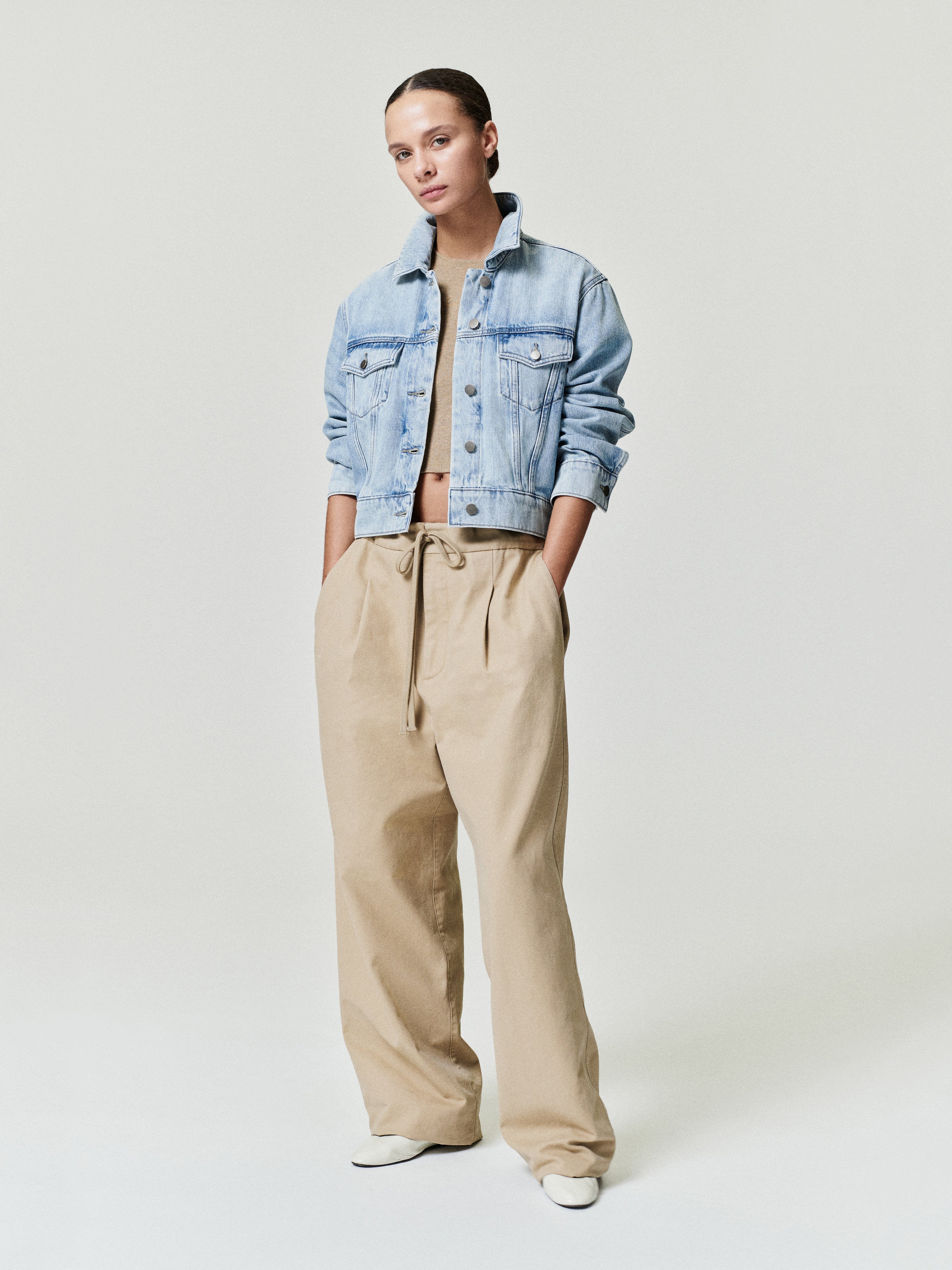woman wearing light blue cropped denim trucker jacket with rolled sleeves and beige wide-leg trousers