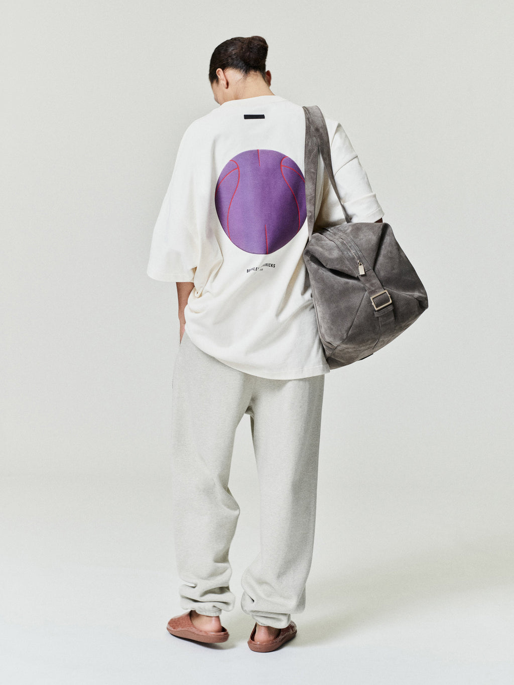person wearing off-white relaxed fit sweatpants paired with oversized white graphic t-shirt and gray suede shoulder bag