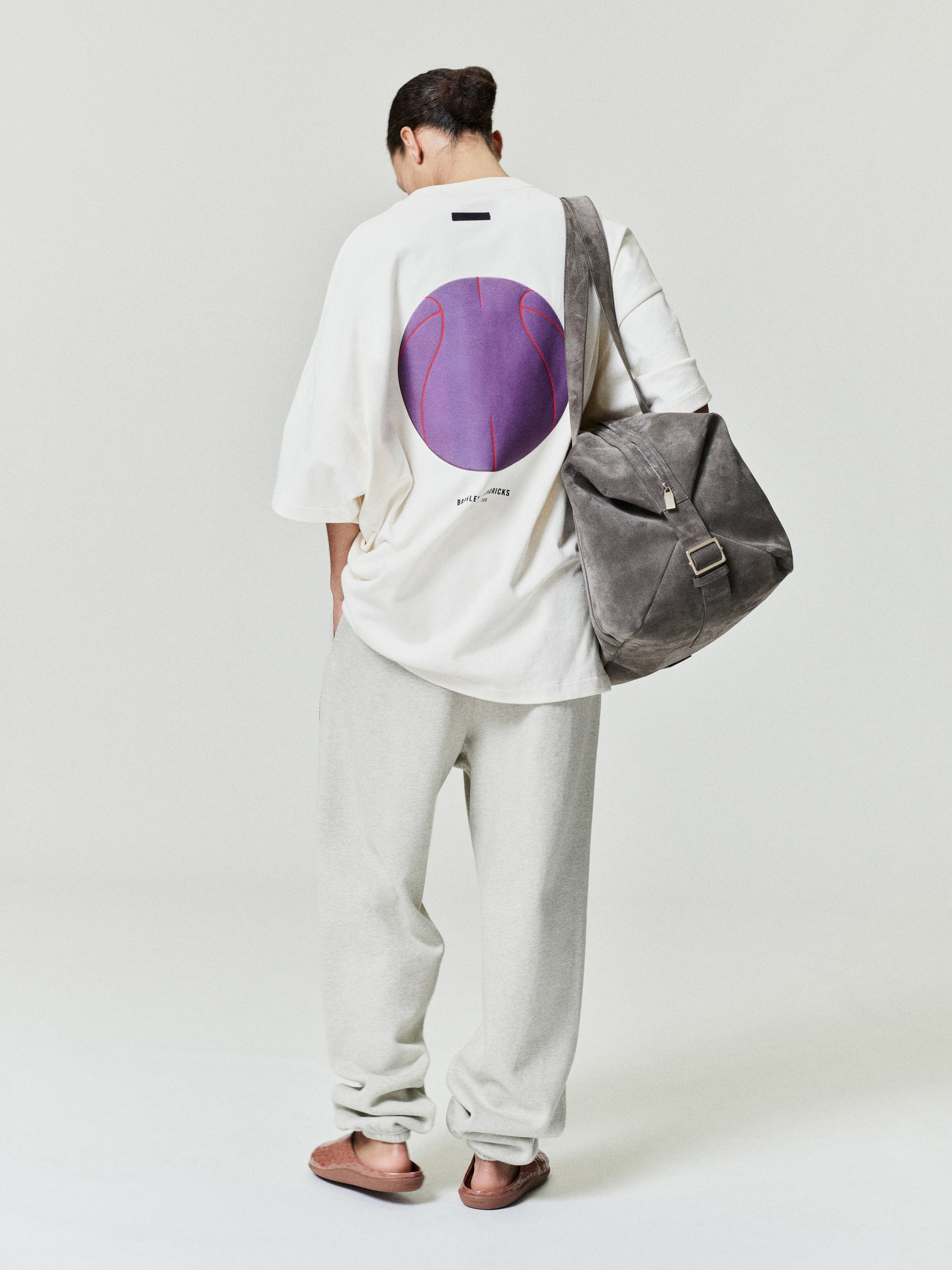 person wearing off-white relaxed fit sweatpants paired with oversized white graphic t-shirt and gray suede shoulder bag