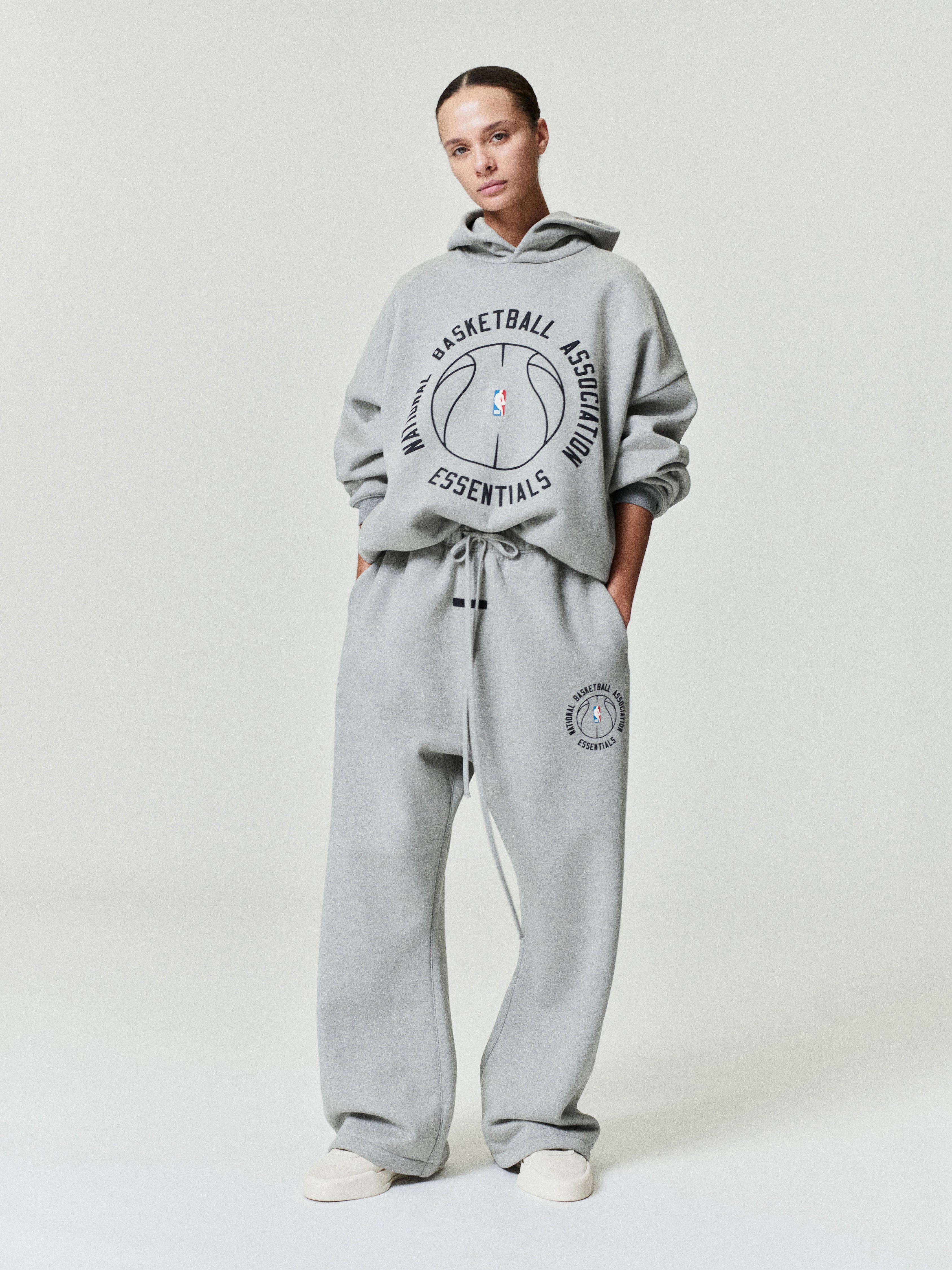 light grey heavyweight hoodie and matching sweatpants with circular NBA Essentials basketball graphics worn by model