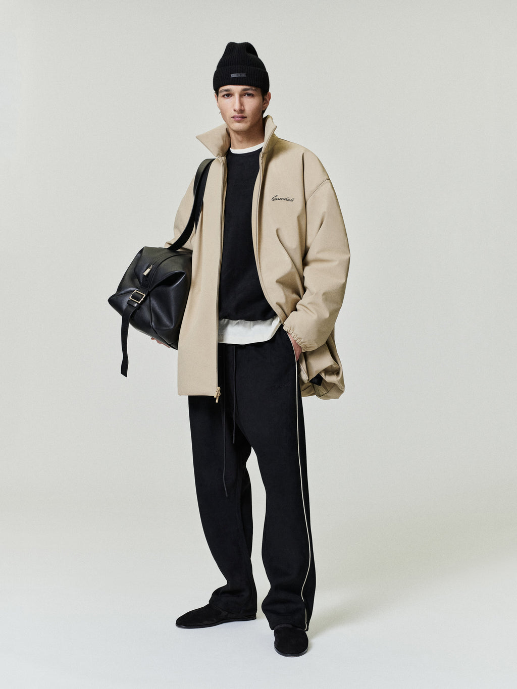 male model wearing black relaxed suede fleece pants with contrasting side piping and a beige oversized jacket