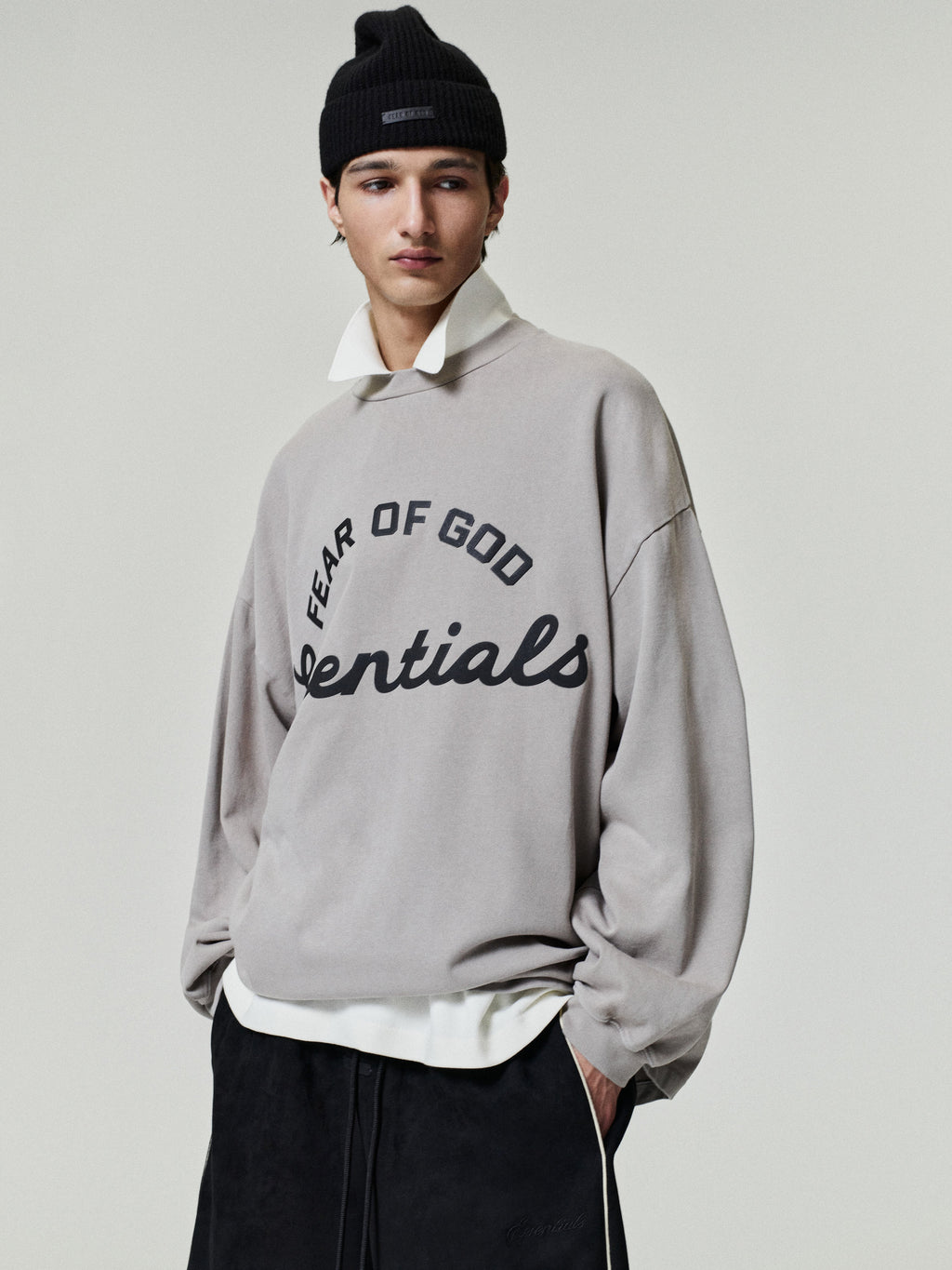 Person wearing a gray 'Fear of God Essentials' sweatshirt on a plain background