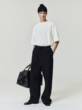 male model wearing oversized white medium-weight cotton poly pique tee with dropped shoulders and black wide-leg pants