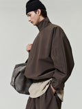 Person wearing a brown jacket and holding a gray bag on a light gray background