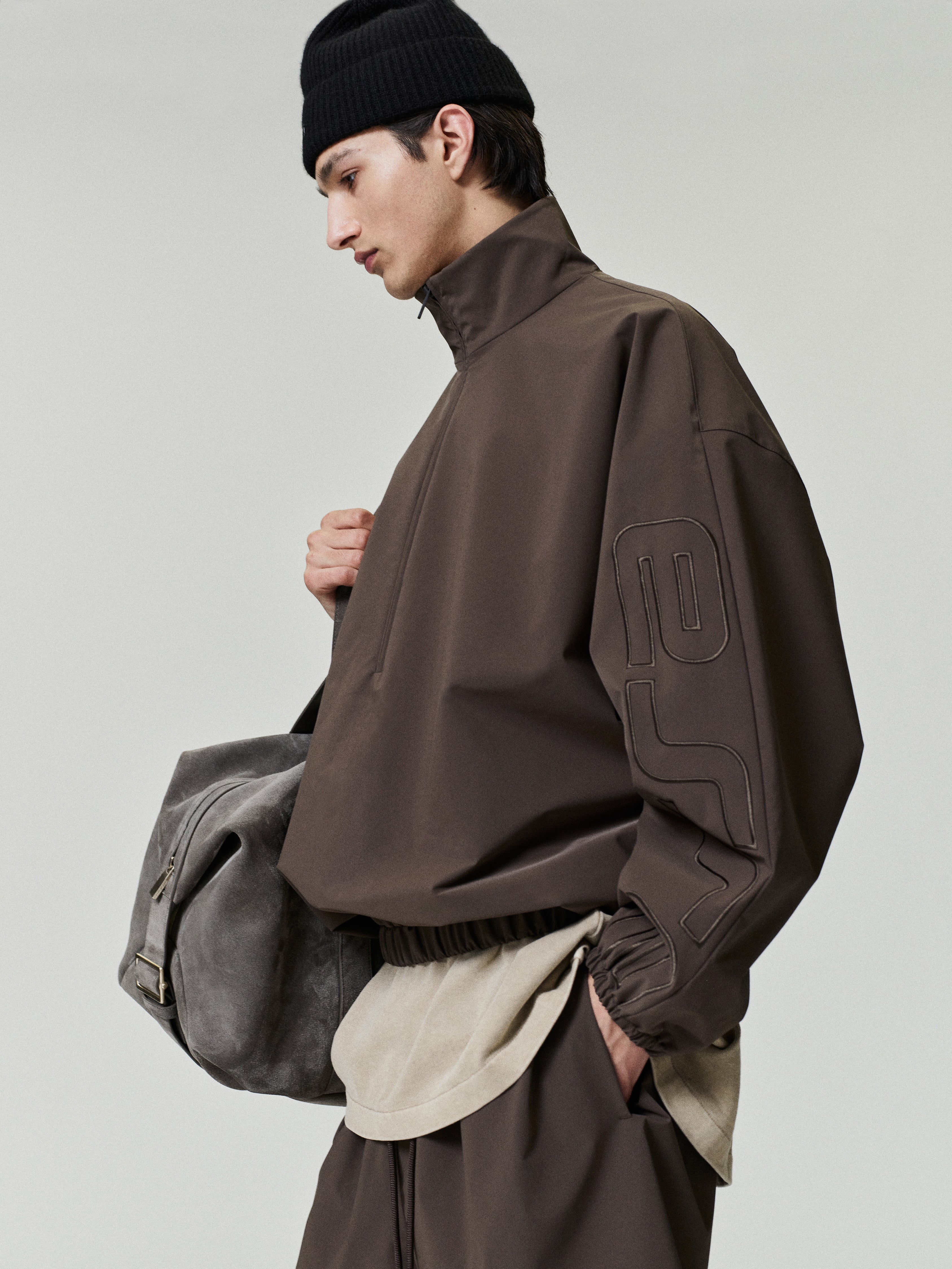Person wearing a brown jacket and holding a gray bag on a light gray background