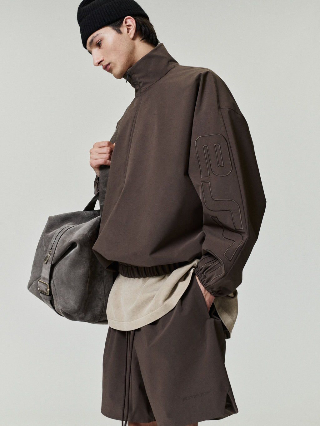 Person wearing a brown jacket and holding a gray bag on a plain background