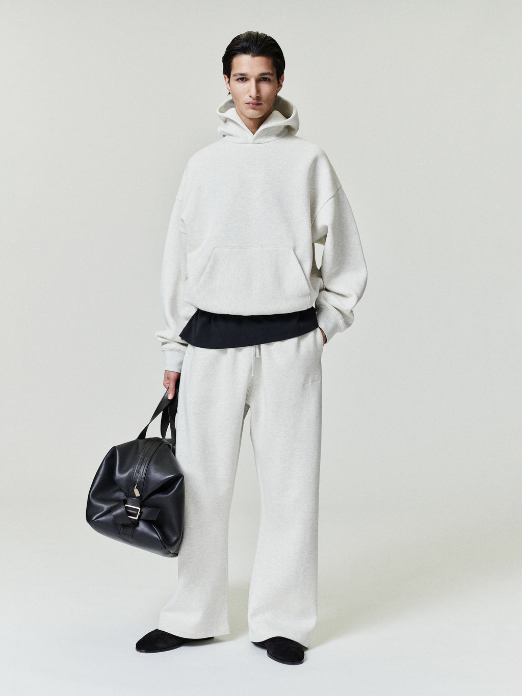 Person wearing a white hoodie and pants holding a black bag on a light gray background