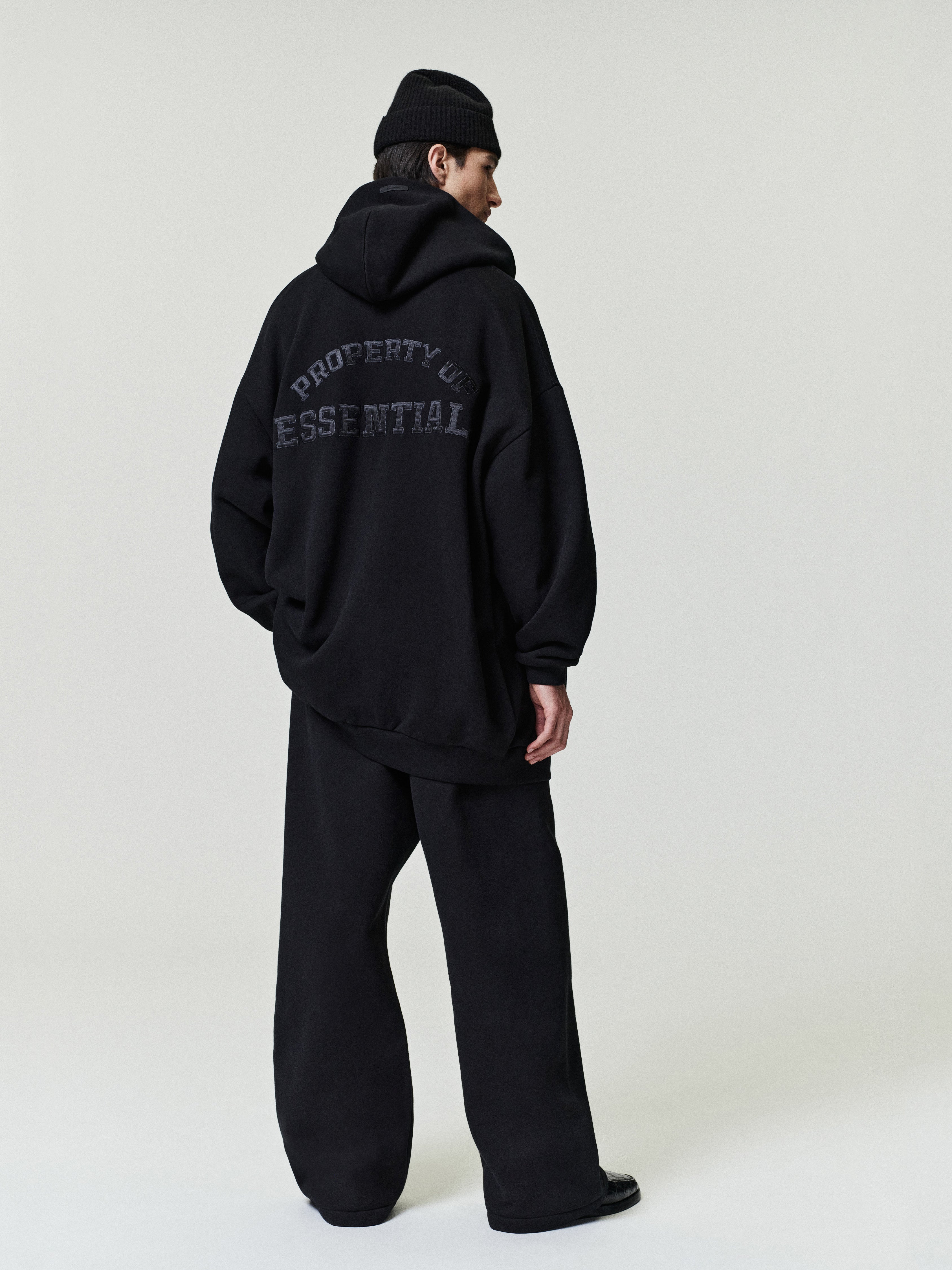 man in oversized black hoodie with graphic text paired with loose black pleated pants and black beanie