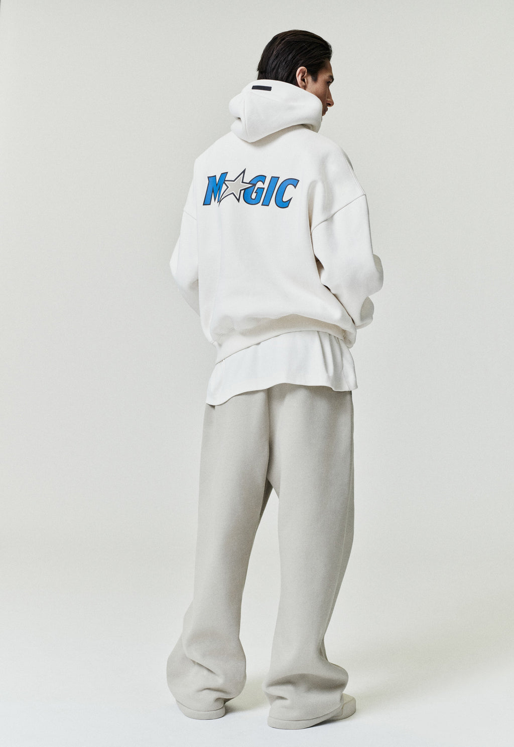 Rear view of white Orlando Magic 90s Hoodie with blue team logo and star detail, model standing, image SP26_F_L64-P_3121