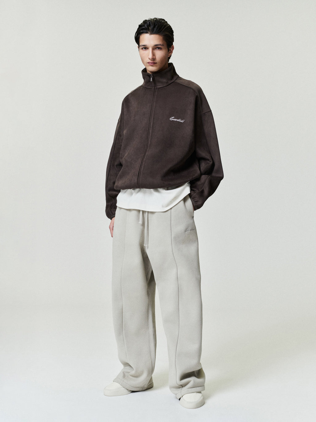 Person wearing a brown fleece jacket and light gray pants on a white background